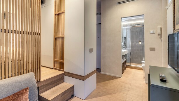 Un intérieur moderne avec un escalier menant à une salle de bain, un canapé avec un coussin et une télécommande posée sur une étagère.