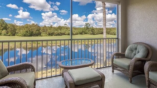 Ein Balkon mit Korbmöbeln, einem Glastisch und Blick auf einen Golfplatz und ein Gewässer.