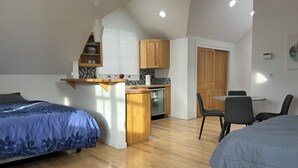 Een kleine kamer met twee bedden, een kitchenette en een eethoek.