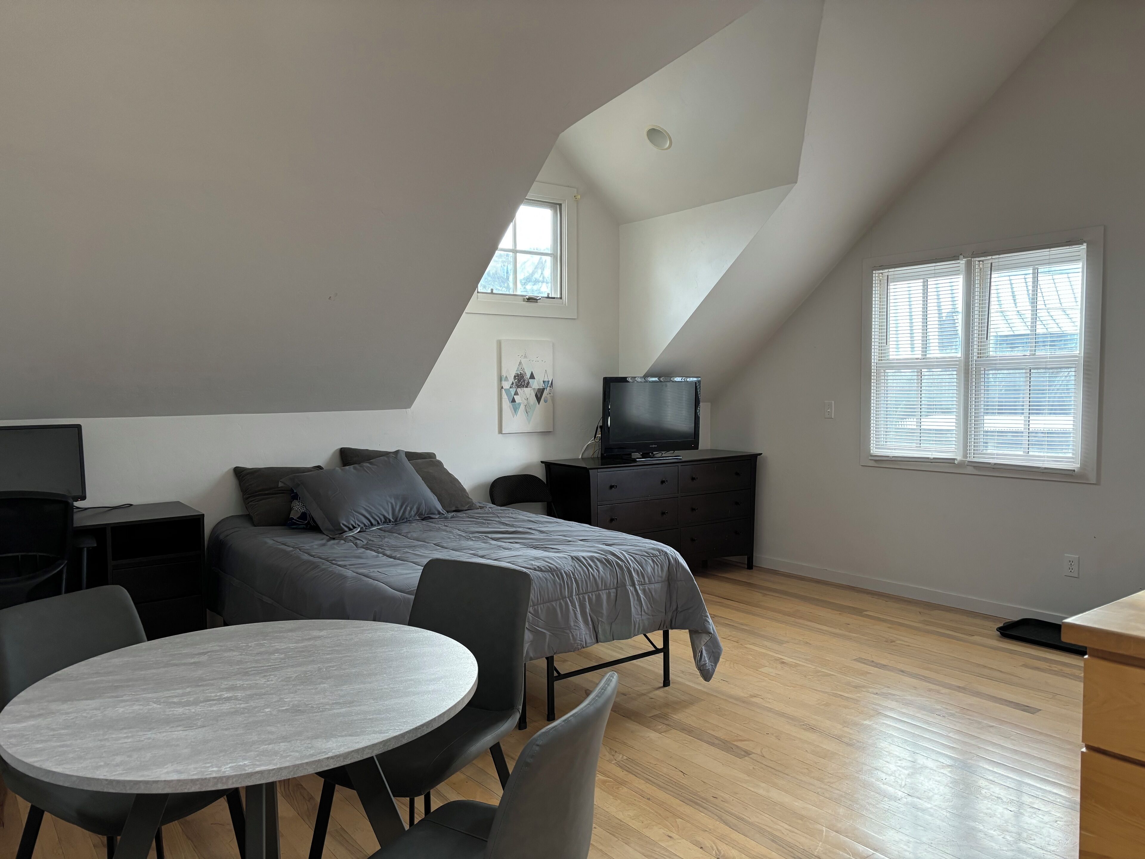 A loft-style bedroom with a bed, a TV, a desk, and a dining table.
