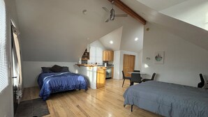 Een slaapkamer in loftstijl met een groot bed, een kleiner bed, een bureau en een kitchenette.