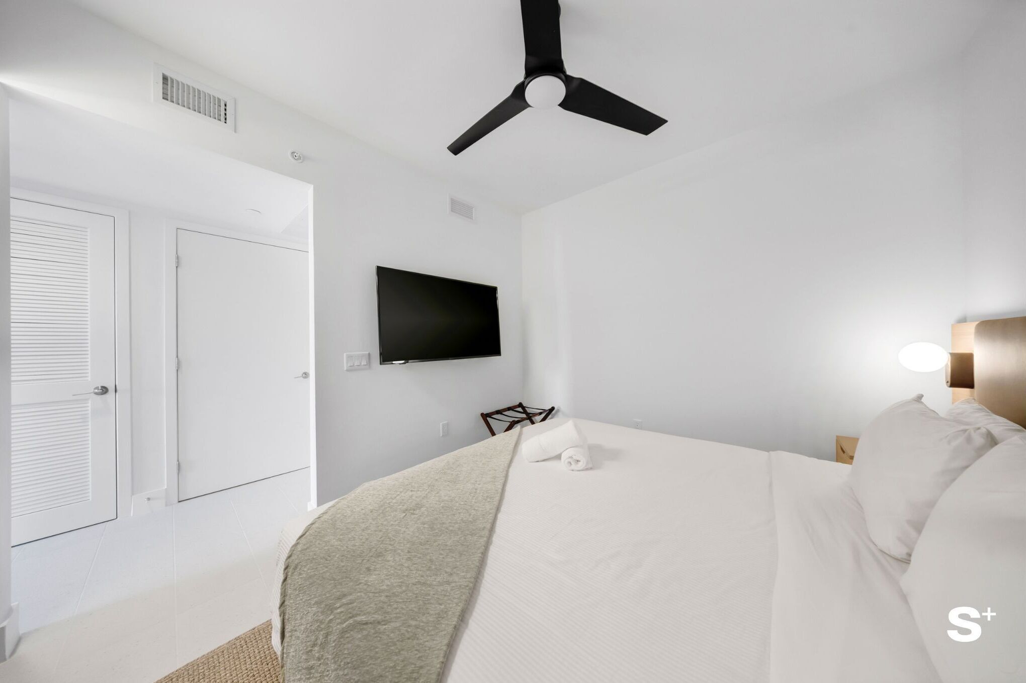 Une chambre d’hôtel équipée d’un lit, d’un ventilateur de plafond, d’un téléviseur à écran plat fixé au mur et d’une table de chevet avec une lampe.