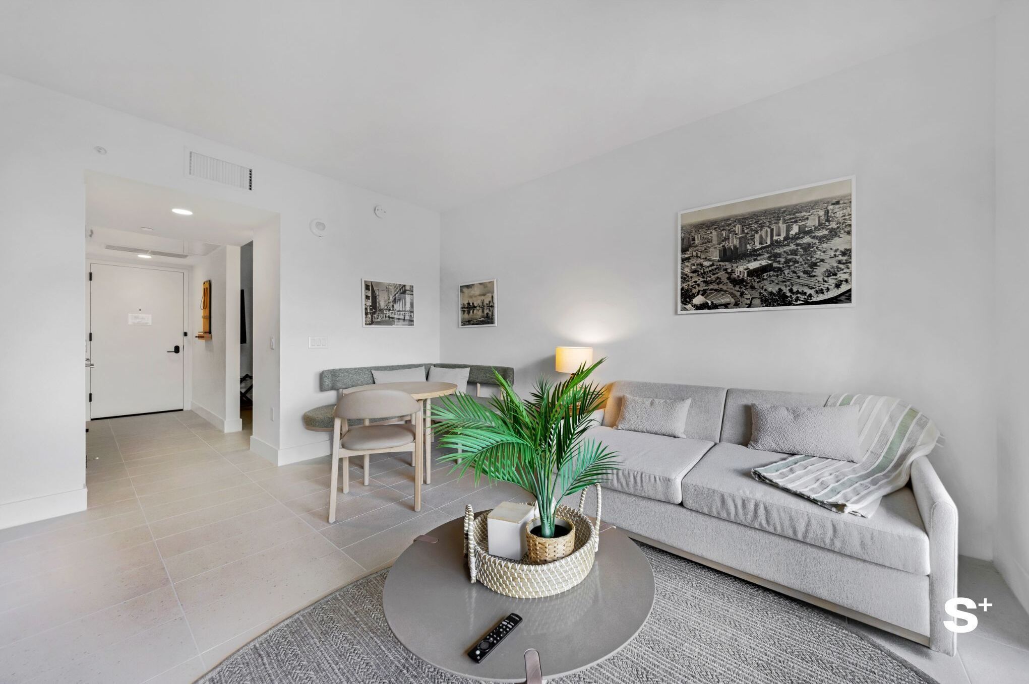 A modern living room with a grey sofa, a round coffee table with a plant, a remote control, and a framed cityscape picture on the wall.