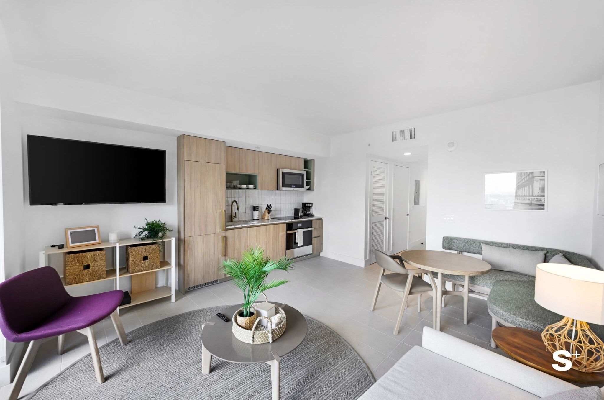 Una sala de estar moderna con un televisor de pantalla plana, un sofá, una mesa de comedor y una cocina con armarios de madera y un microondas.