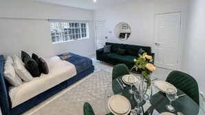A modern living room with a sofa, a dining table set for two, and a large window with a view. - Sleek studio flat near King’s Cross, St Pancras, Euston with Free Wi-Fi (London)