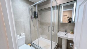 A modern bathroom with a glass-enclosed shower, a white toilet, and a sink with a mirror above it. - Sleek studio flat near King’s Cross, St Pancras, Euston with Free Wi-Fi (London)