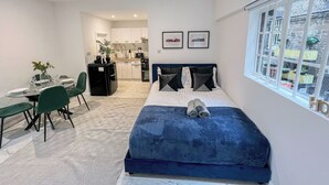 A compact bedroom with a bed, a dining table with chairs, a kitchenette, and a window with a view. - Sleek studio flat near King’s Cross, St Pancras, Euston with Free Wi-Fi (London)