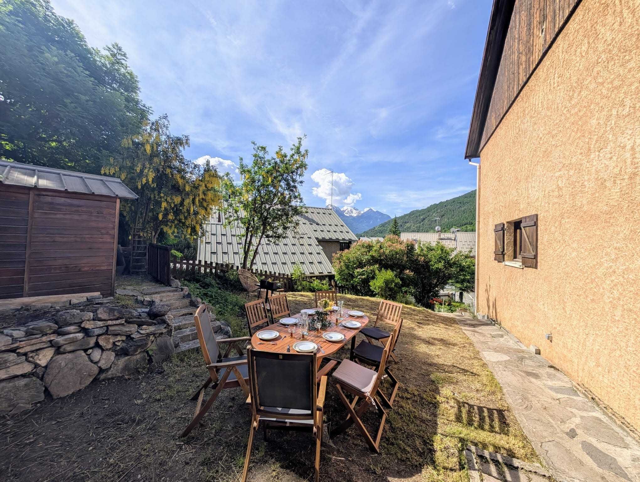 Un espace de restauration en plein air avec un mur en pierre, des chaises en bois et une table dressée pour quatre personnes.
