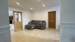 A spacious living room with a grey sectional sofa, a wooden door, and a tiled floor. - Rostrevor Valley Hometel (Newry)