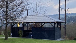 A covered outdoor seating area with a roof, surrounded by grass and trees. - Rostrevor Valley Hometel (Newry)