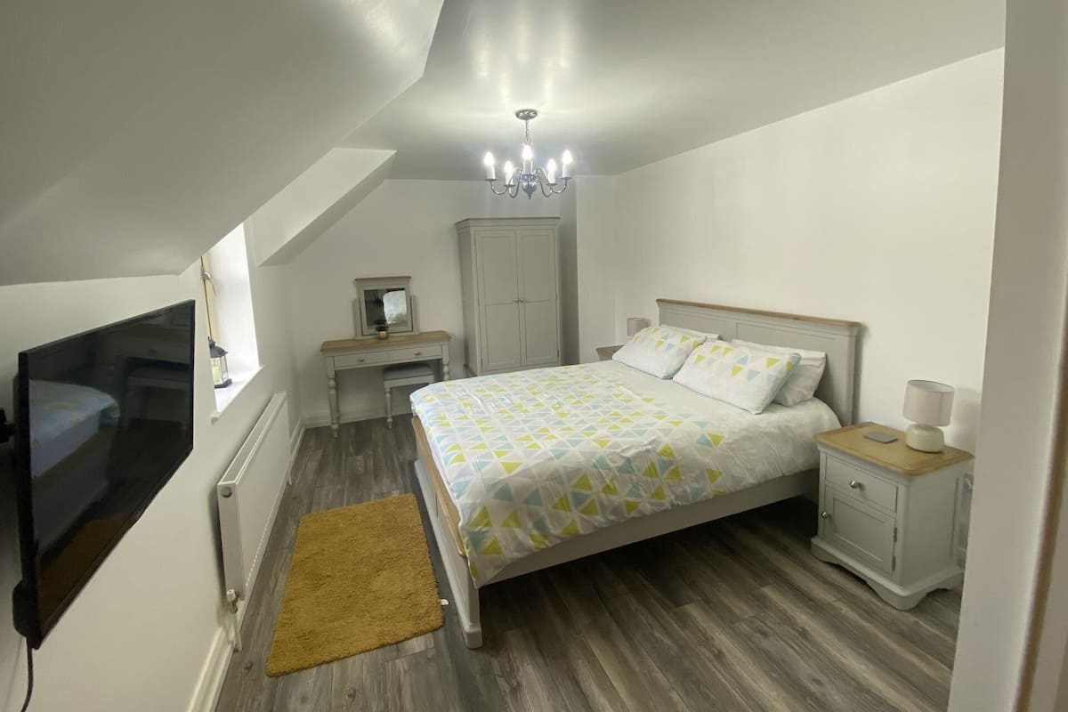 A bedroom with a bed, nightstands, a dresser, a mirror, a chandelier, and a TV.