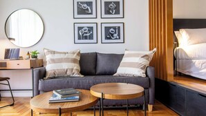 A modern living room with a grey sofa, two round wooden tables, a round mirror, and four framed black and white photographs on the wall. - Premium Depto con jardin Palermo C1A (Buenos Aires)