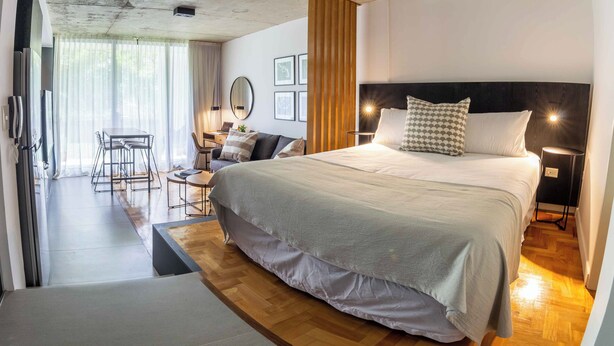 A modern bedroom with a large bed, bedside lamps, and a view of a dining area. - Premium Depto con jardin Palermo C1A (Buenos Aires)