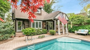 A house with a swimming pool, a covered patio, and a garden with red maple leaves.