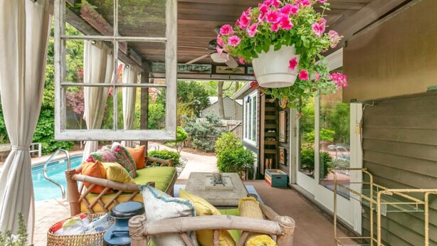 A covered outdoor seating area with a pool, wicker furniture, and hanging flower baskets.