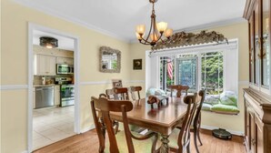 A dining area with a wooden table and chairs, a chandelier, and a view of the garden through a window.