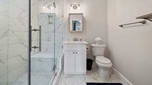 A modern bathroom with a glass shower enclosure, white marble tiles, a white sink with a mirror above, and a toilet. - Modern Chic Retreat in the Heart of EaDo, Houston (Houston)