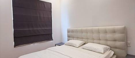 A modern bedroom with a large bed, a bedside table, and a window with blinds.