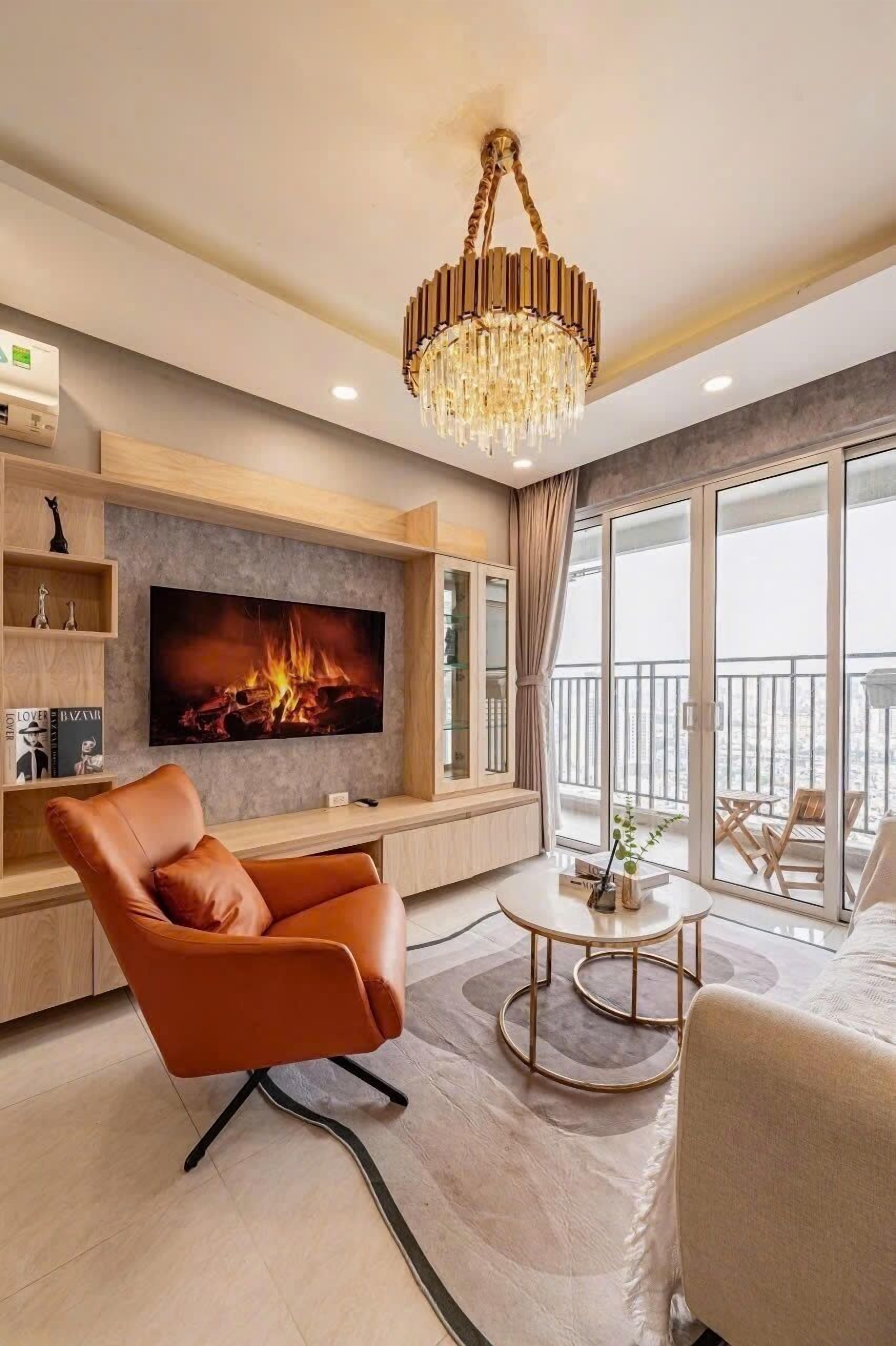 A modern living room with a large flat-screen TV, a leather armchair, a round coffee table, and a chandelier.