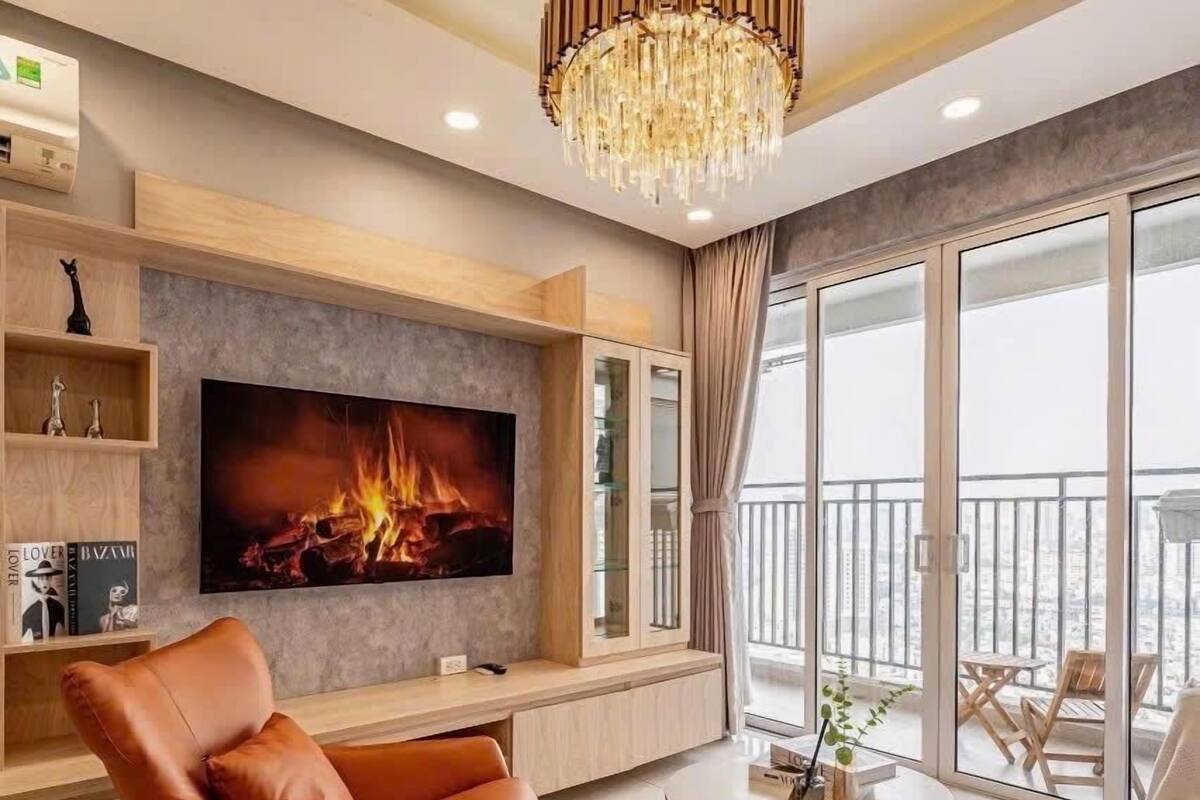 A modern living room with a large flat-screen TV, a leather armchair, a round coffee table, and a chandelier.