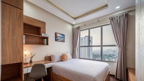 A modern bedroom with a large bed, a desk, and a view of a cityscape through a large window.