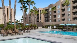 A hotel pool area with lounge chairs, palm trees, and a large building in the background. - 2 Bedroom 2 Bath Condo in Oceanside Within Walking Distance to Ocean and Dining (Oceanside)