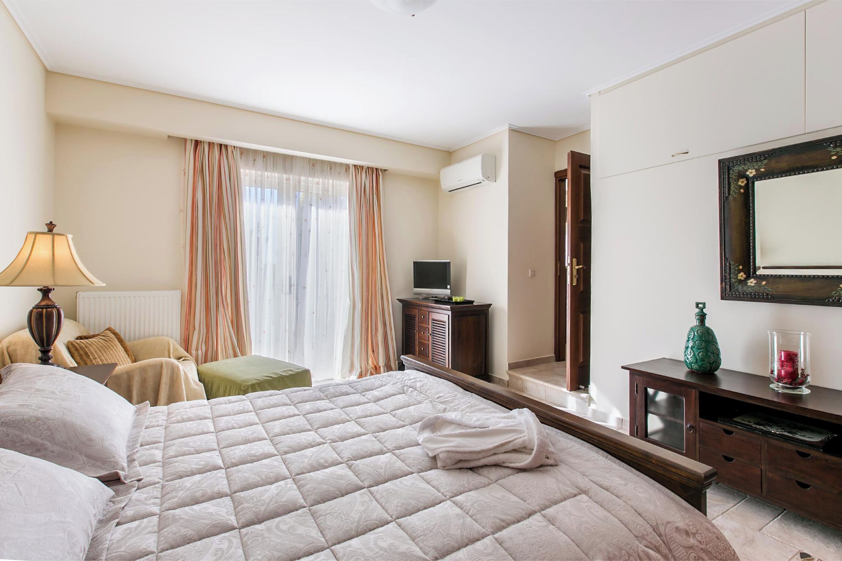 Een hotelkamer met een groot bed, een bureau met een televisie, een dressoir en een spiegel aan de muur.