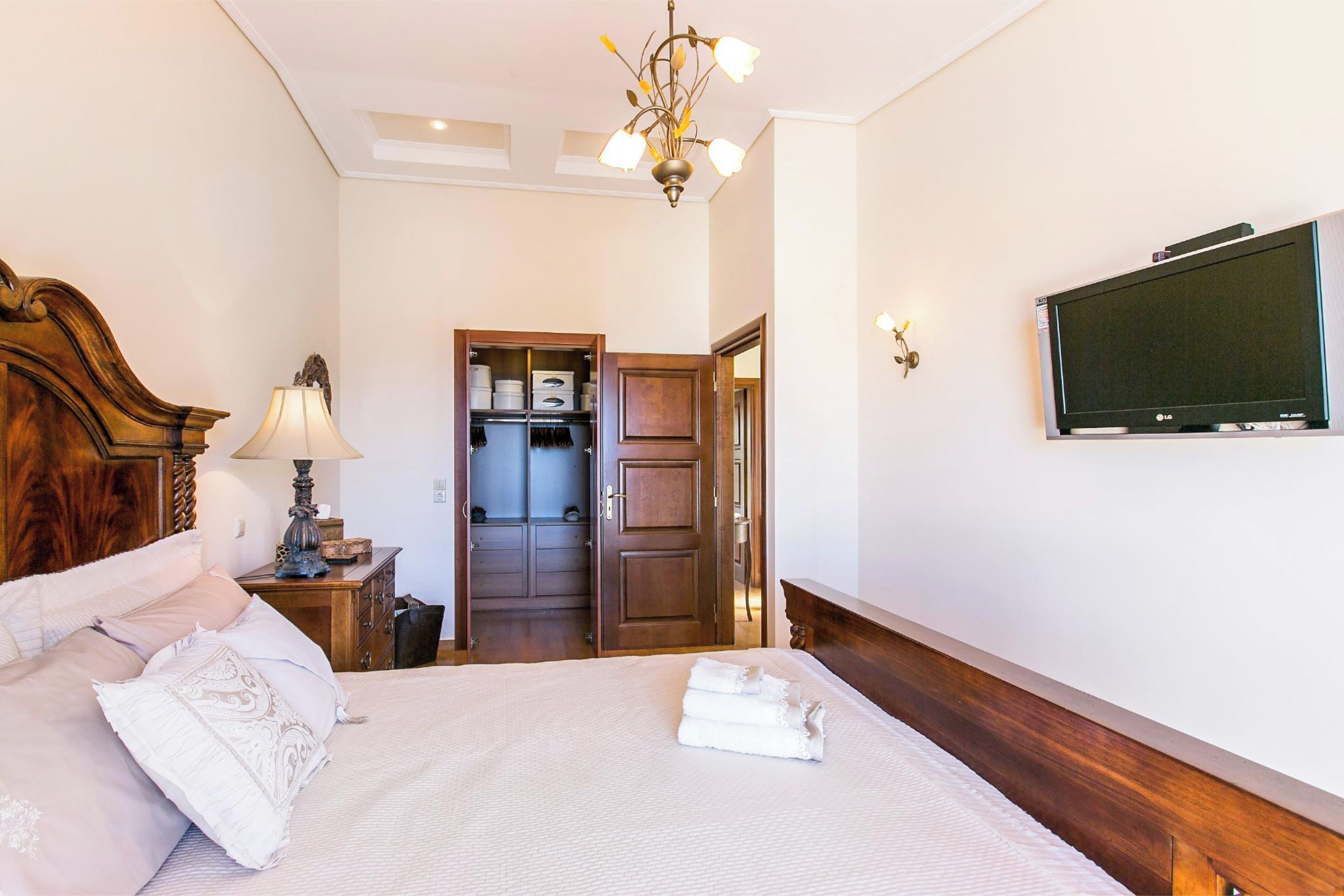 Une chambre d’hôtel bien rangée, avec un lit, une télévision, une tête de lit en bois, une lampe et une armoire.