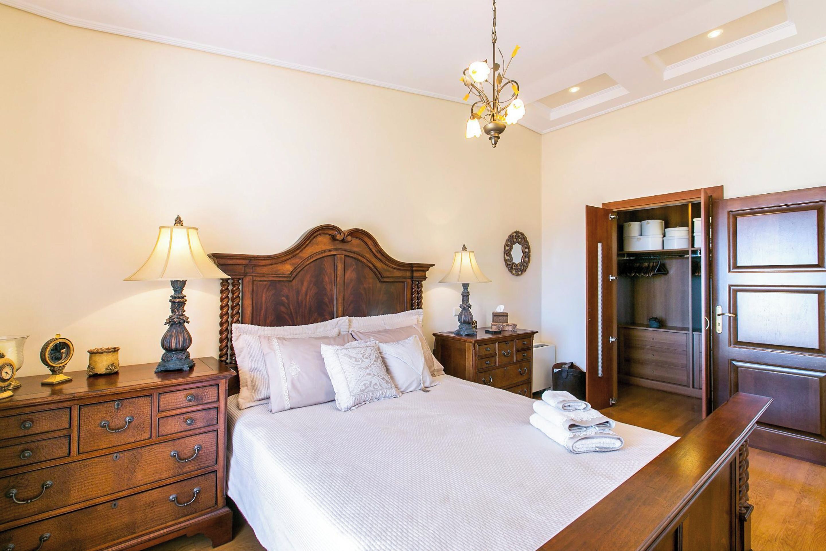 A neatly arranged bedroom with a wooden bed, bedside lamps, a dresser, and a wardrobe.