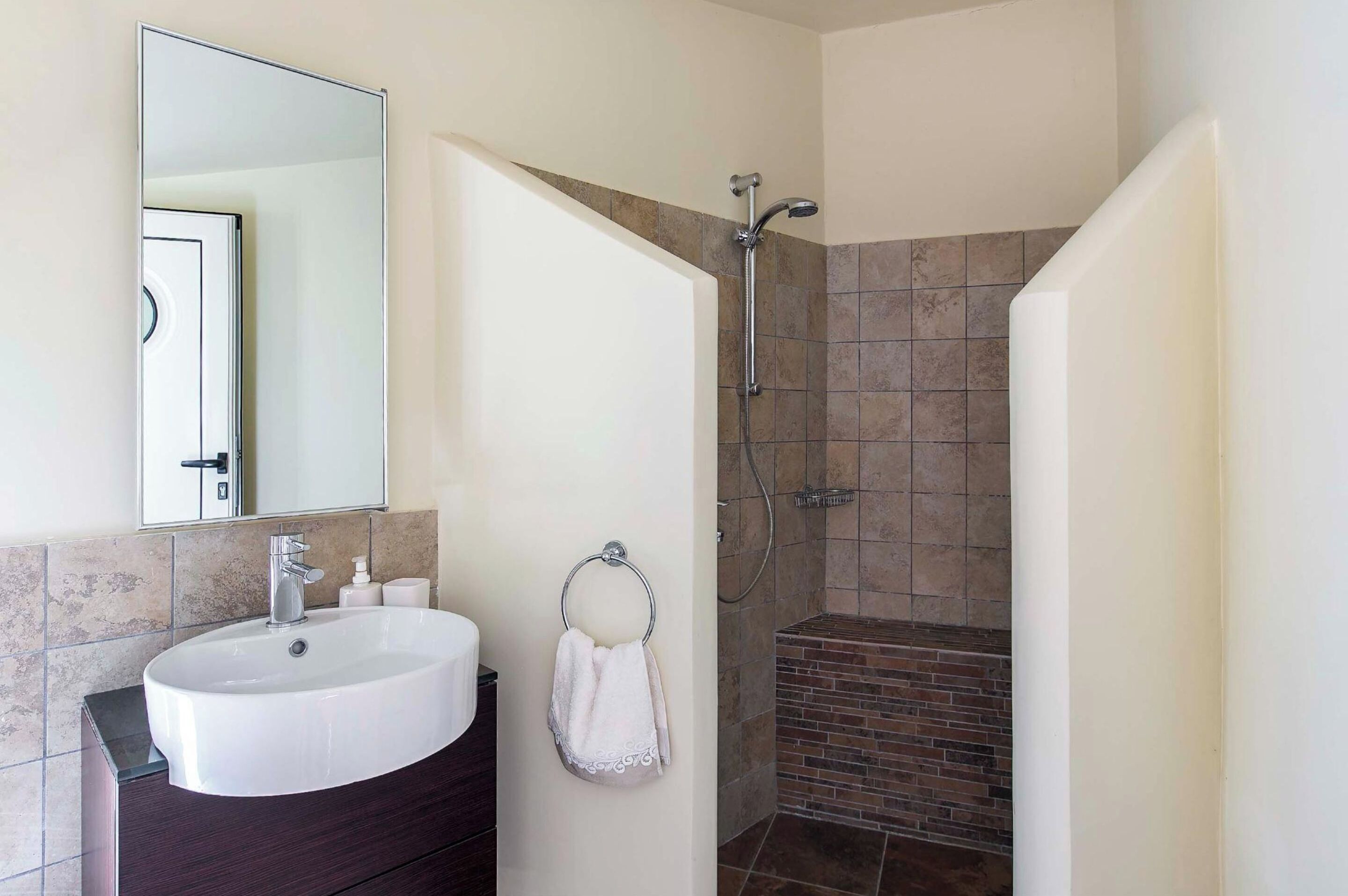 A bathroom with a white sink, a mirror, a towel rack, and a shower area with tiled walls.