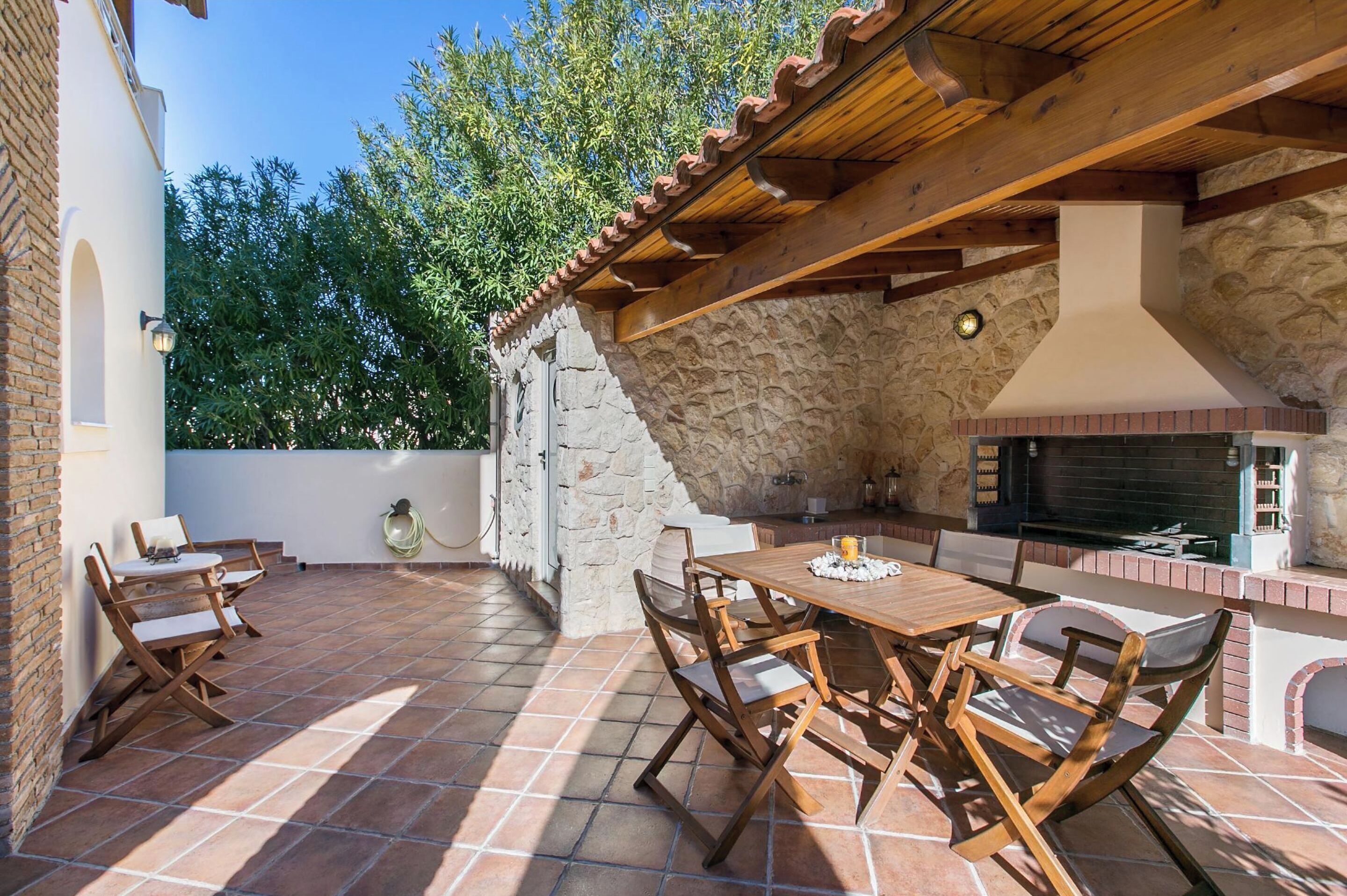An outdoor patio with a brick floor, wooden furniture, and a stone wall.