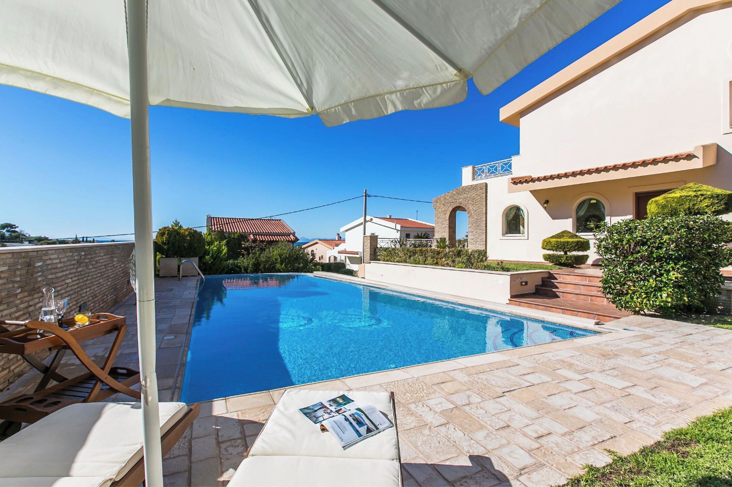 A swimming pool with lounge chairs and a table, surrounded by a patio area with a white umbrella.