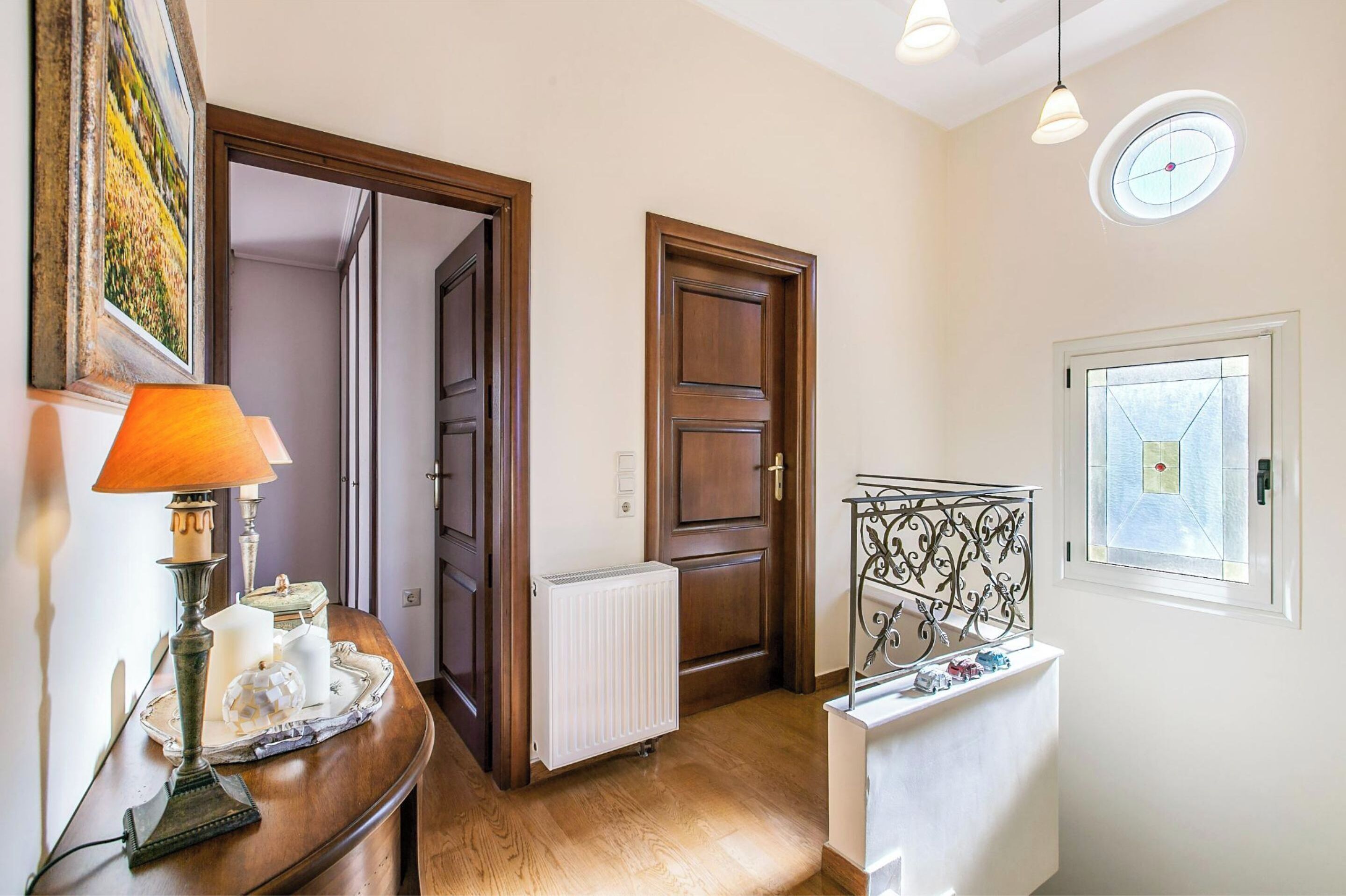 Un pasillo con puertas de madera, un radiador, una lámpara, una bandeja con velas y una ventana con vistas.