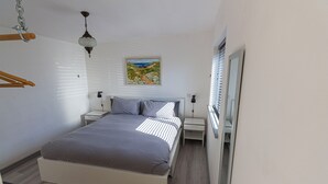 Un dormitorio con una cama, mesitas de noche, una lámpara colgante, un cuadro y una ventana con persianas.