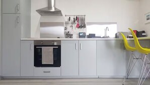 Una cocina moderna con gabinetes blancos, una campana extractora de acero inoxidable y un horno empotrado. Se observan utensilios colgando y un lavamanos pequeño con grifo.
