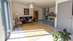 Una sala de estar moderna con sofá, mesa de centro y estantería. Cuenta con una zona de cocina con armarios y mesa de comedor.