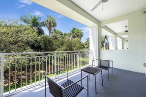 A balcony with two metal chairs, a white railing, and a view of greenery and palm trees. - Two-Level Town House-Doral location-We Host (Miami)
