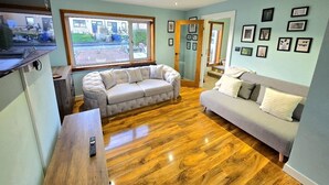 A living room with two sofas, a wooden floor, and a TV on a stand. - Quirky 2-Bed with Free Parking (Paisley)