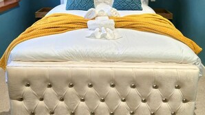A large bed with a tufted headboard, two pillows, and a yellow throw blanket. - Quirky 2-Bed with Free Parking (Paisley)