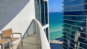 Un balcon avec vue sur l’océan et une plage, une chaise et une table.
