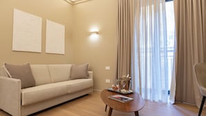 Ένα μοντέρνο σαλόνι με έναν μπεζ καναπέ, ένα ξύλινο τραπεζάκι σαλονιού και ένα μεγάλο παράθυρο με λεπτά, διάφανα κουρτίνες.