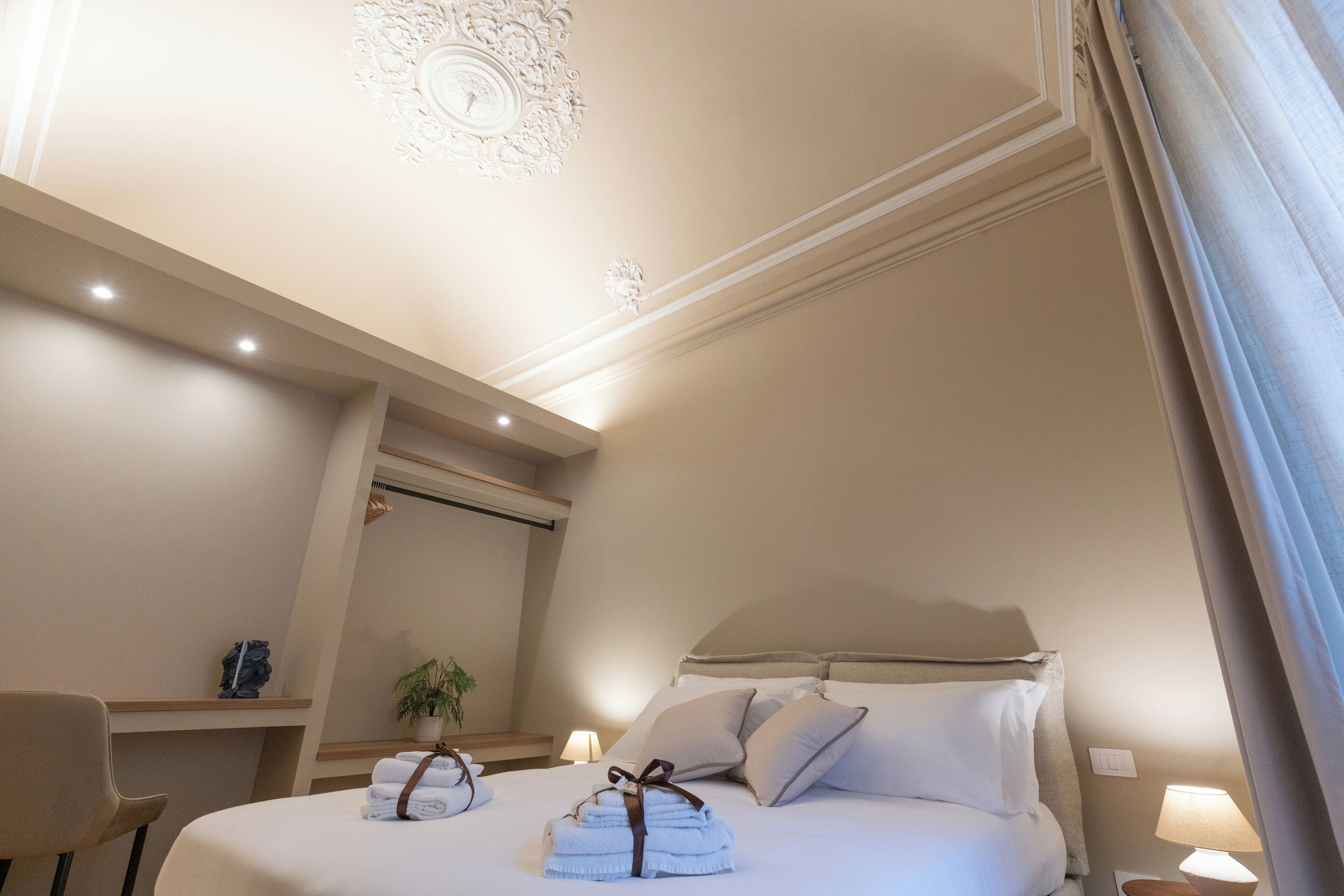 Une chambre d’hôtel avec un lit bien fait, une table de chevet avec une lampe, une petite plante et un luminaire décoratif au plafond.