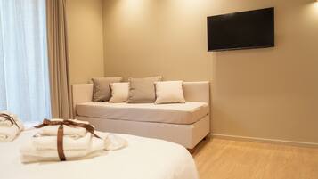 Quarto de hotel com cama, sofá, televisão de tela plana e janela com cortinas.