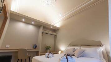 A hotel room with a bed, a desk, a chair, a potted plant, and a ceiling light fixture.