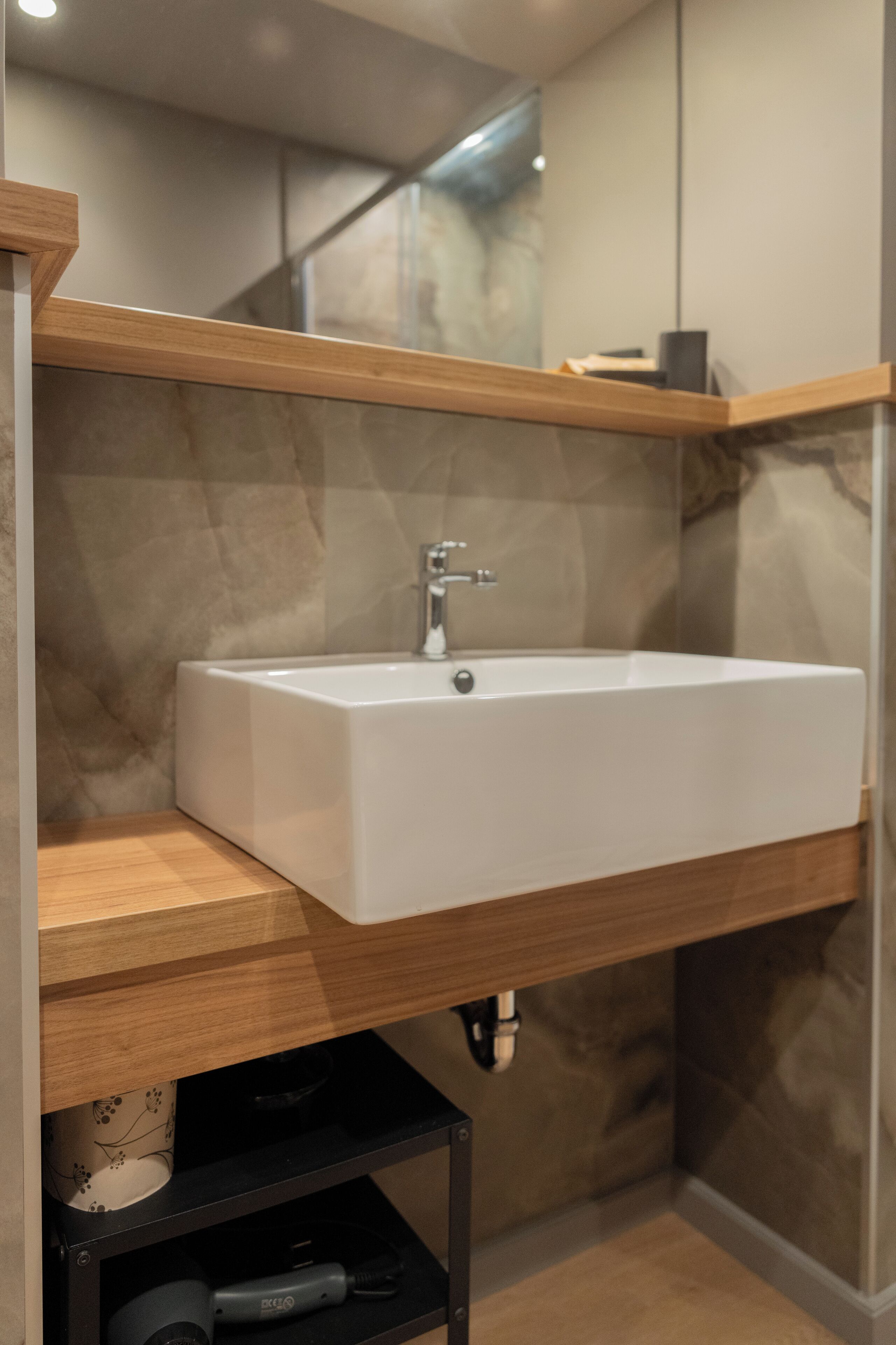 Une salle de bain moderne avec un lavabo blanc, un plan de toilette en bois et un pare-feu en marbre.