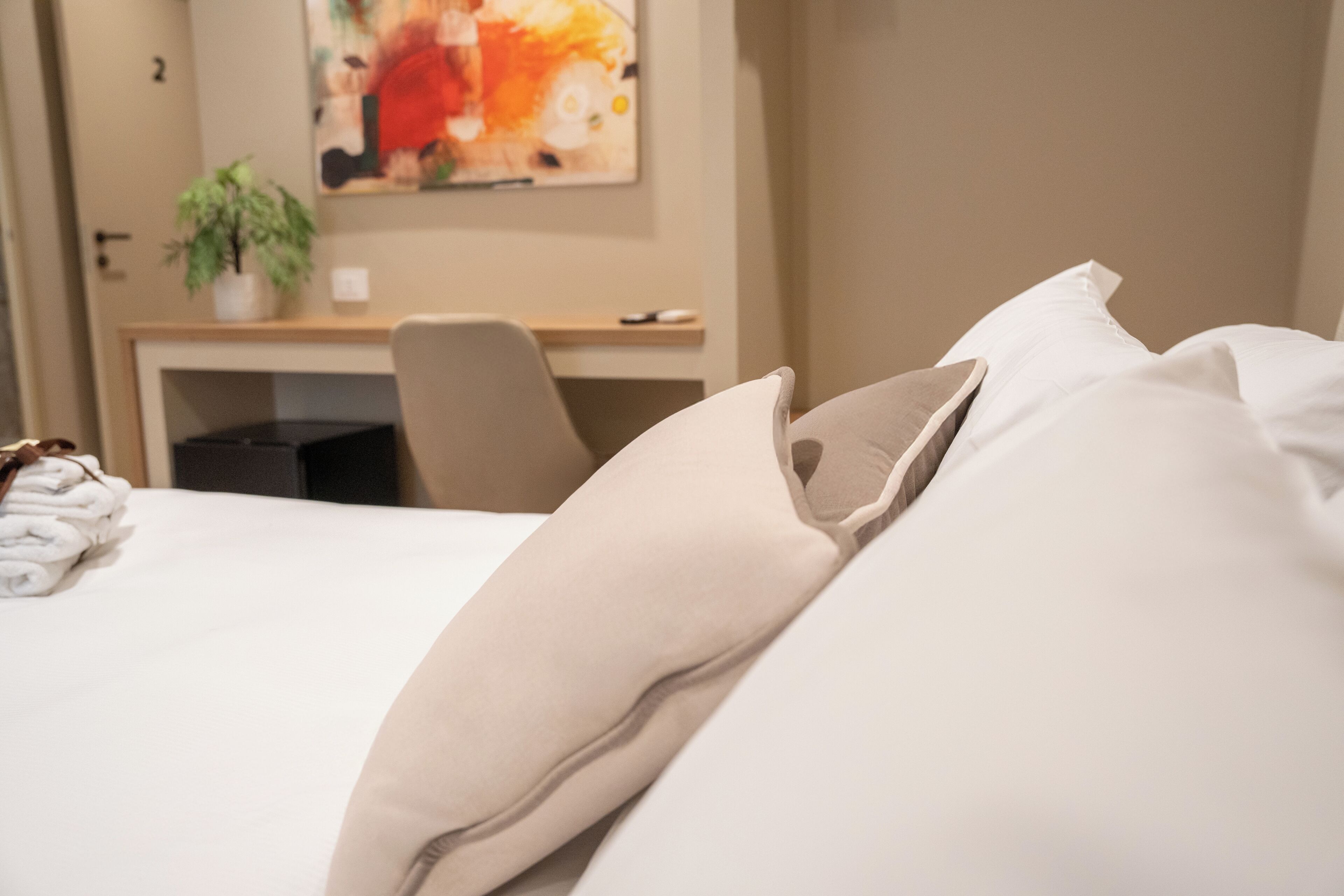 Una habitación de hotel con una cama bien hecha, un escritorio con un ordenador y un cuadro en la pared.