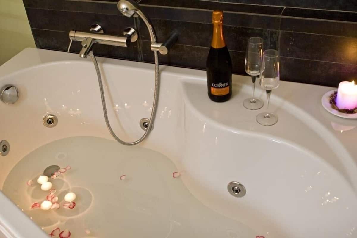 A bathtub with a champagne bottle and glasses, surrounded by rose petals.