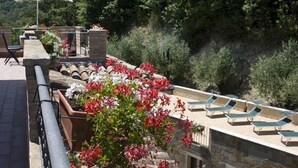 Terraza en la azotea con sillones, una sombrilla blanca y macetas de flores.