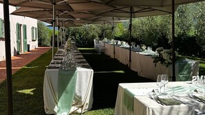 Un espacio para eventos al aire libre con mesas dispuestas bajo sombrillas grandes, organizadas en filas con sillas.