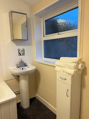 A bathroom with a white sink, a mirror, a window with frosted glass, and a towel rack with folded towels. - Stylish 2 Bedroom Apartment in Havant (Havant)